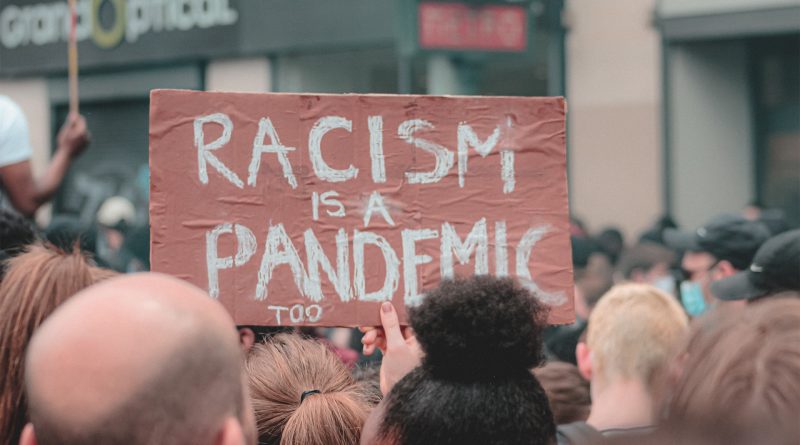 Schild bei einer Demonstration: "Racism is a Pandemic too"