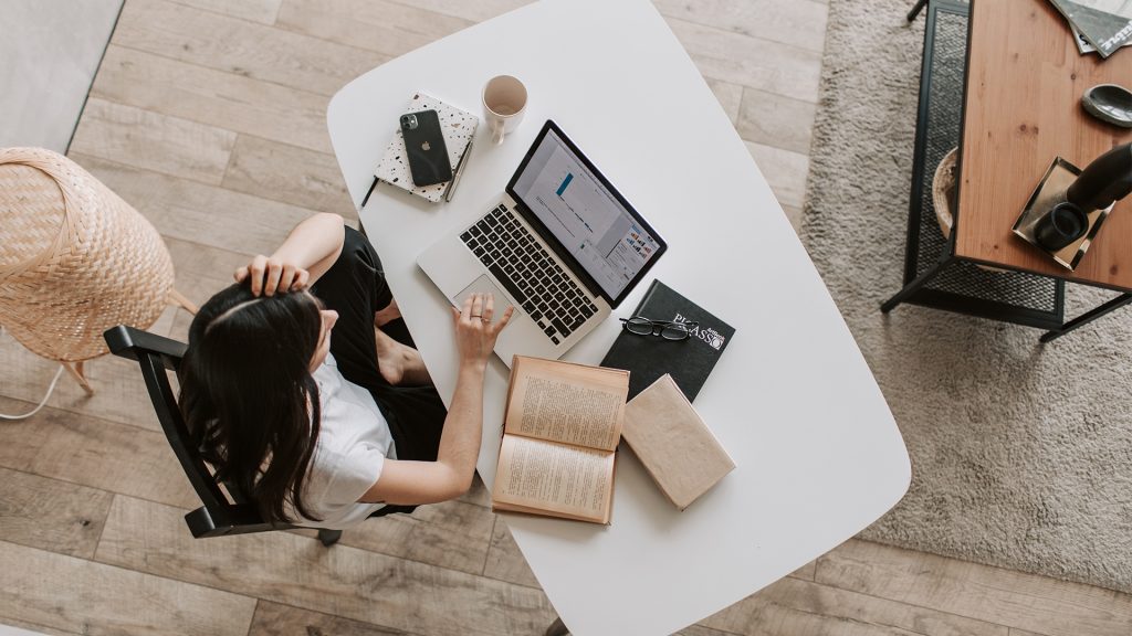 Frau im Homeoffice, Foto von oben, Laptop, Bücher liegen auf einem Tisch