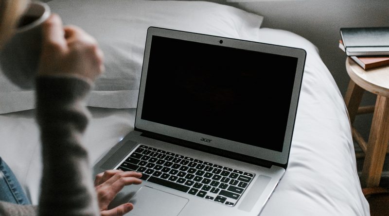 Frau trinkt aus einer Tasse auf dem Bett sitzend, davor ein Laptop, Bildschirm schwarz