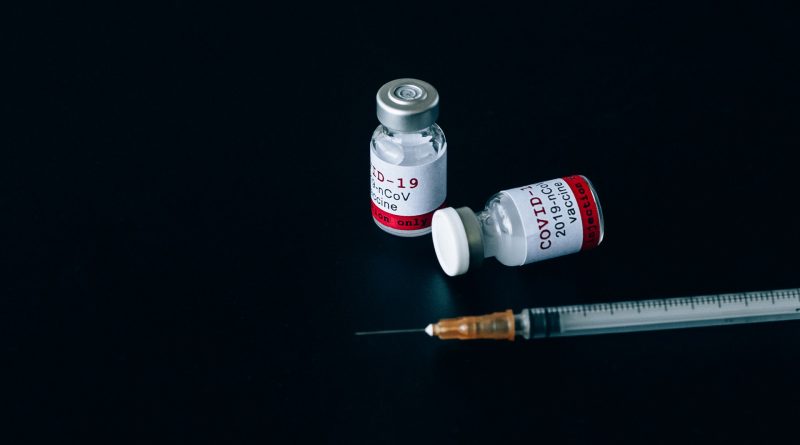 Impfstoff gegen Covid-19 mit Spritze auf schwarzem Untergrund