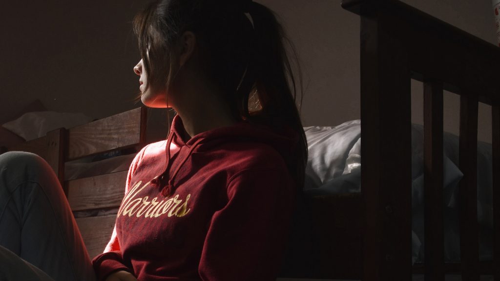 Frau mit Pullover-Aufschrift "Warrior" sitzt auf dem Boden vor einem Bett
