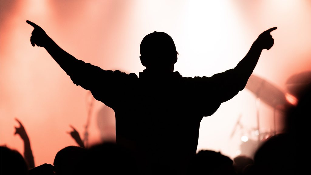 Silhouette eines Menschen bei einem Konzert, streckt die Arme in die Höhe