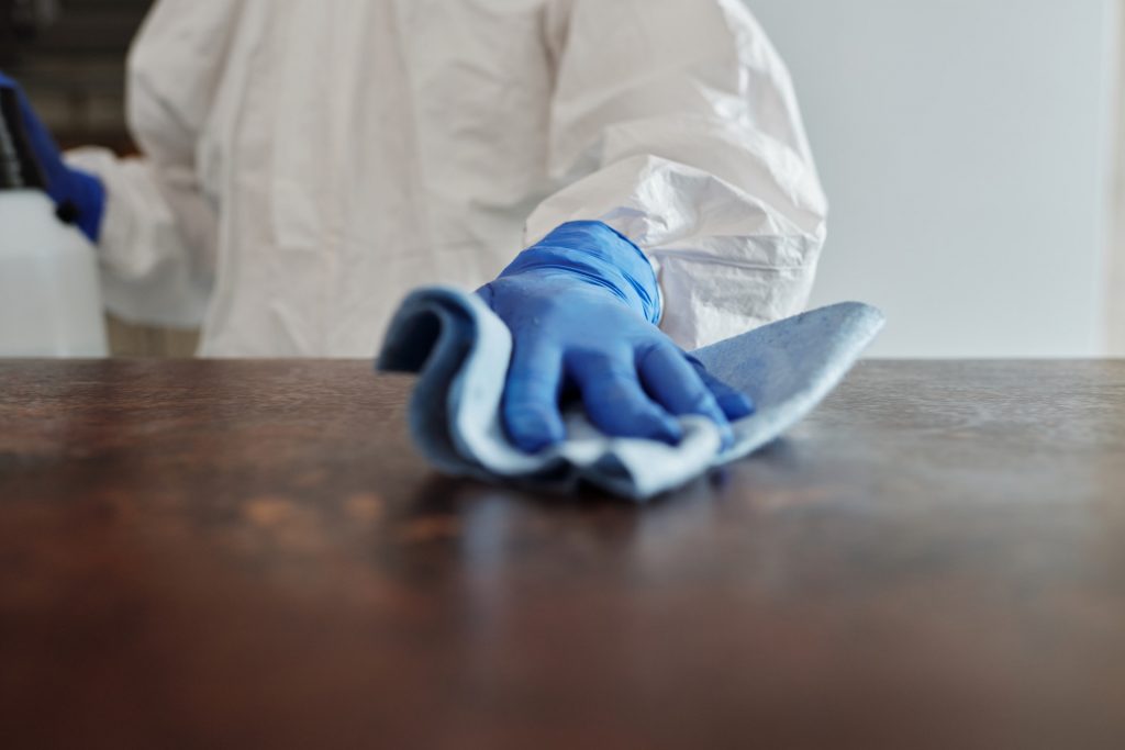 Mensch mit Handschuhen putzt Tisch