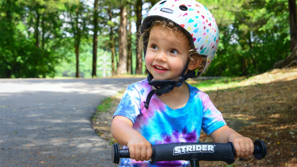 Kind mit Radhelm lächerlt, Hintergrund Wald
