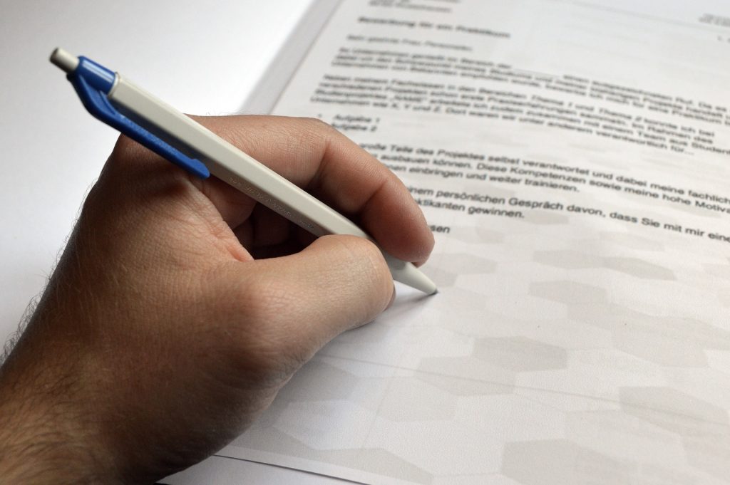 Hand mit KUgelschreiber schreibt auf Blatt Papier
