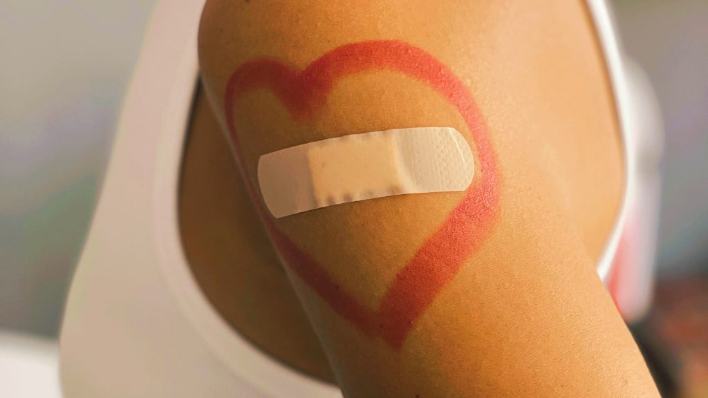 Arm, auf dem ein rotes Herz gemalt ist, in dem ein Pflaster klebt