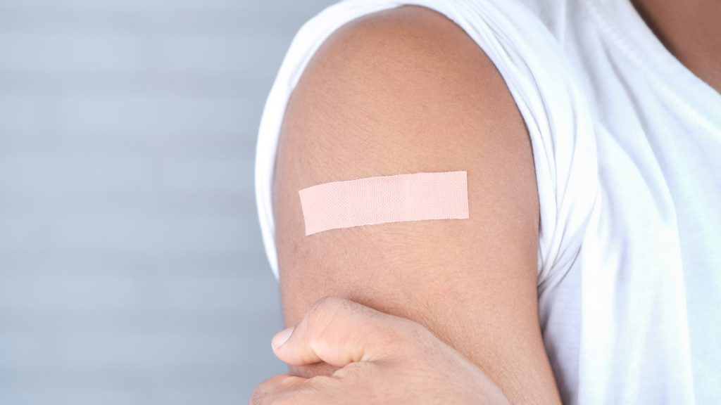 Mensch mit weißem Shirt trägt Pflaster auf dem Arm