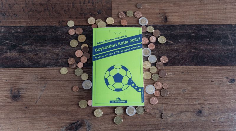 Das Buch "Boykottiert Katar 2022!" liegt auf einem Holztisch, umringt von Münzen