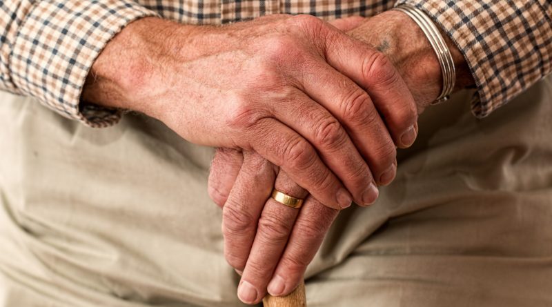 Hände eines alten Menschen mit Ring am Finger halten einen Stock