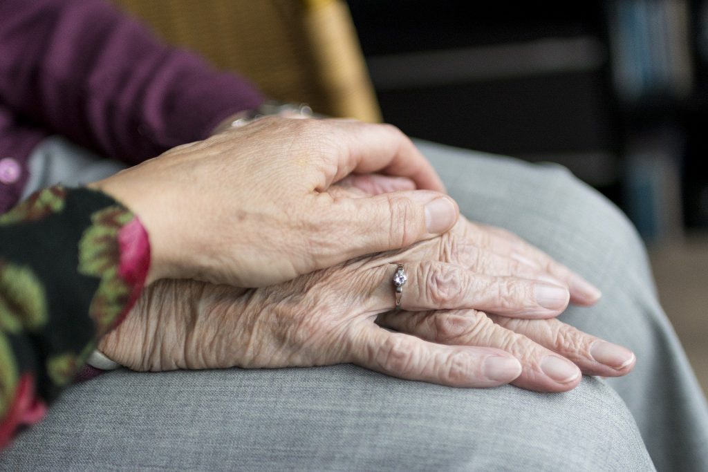 Hand einer jüngeren Person liegt auf der Hand einer alten Person