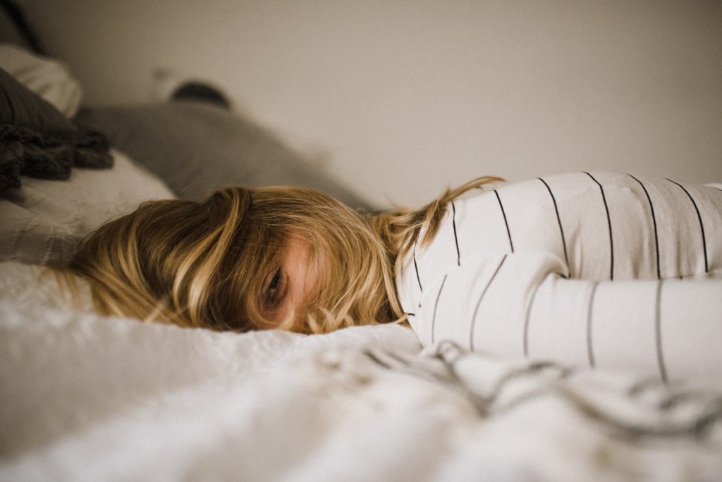 Frau mit blonden Haaren und weißem Shirt liegt auf auf dem Bett
