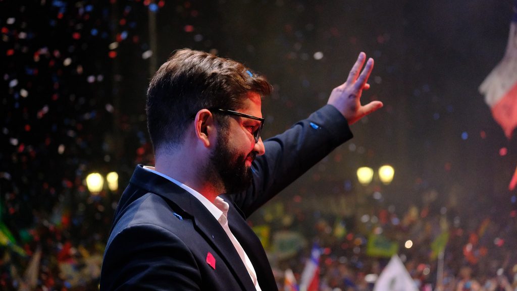 Gabriel Boric mit erhobener linker Hand, winkt dem Publikum zu