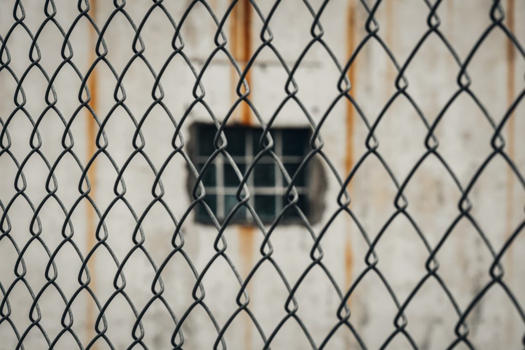 Gefängnisfenster hinter einem Maschendrahtzaun