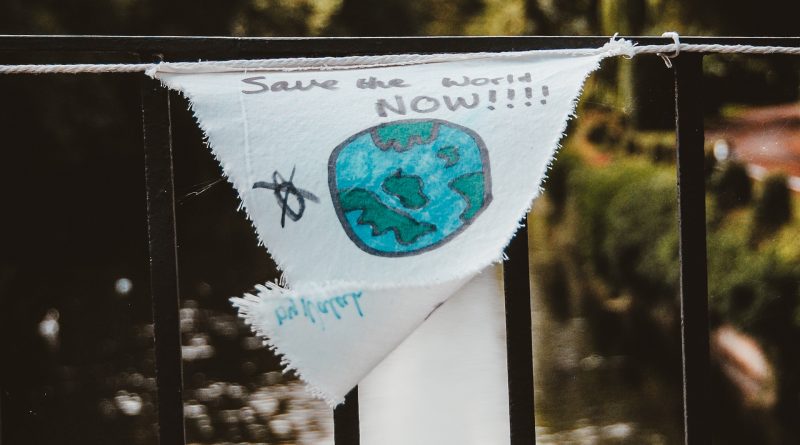 Weißes Stück Stoff mit Aufschrift "Save the World NOW!!!" hängt an einem Brückengeländer