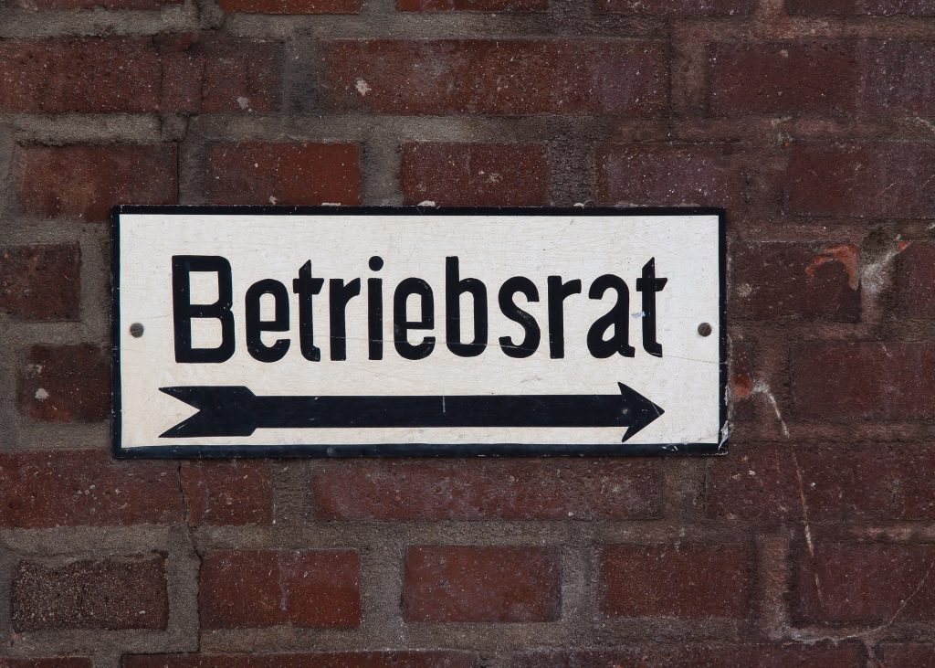 Schild mit der Aufschrift "Betriebsrat" mit Pfeil nach rechts auf einer Backsteinmauer