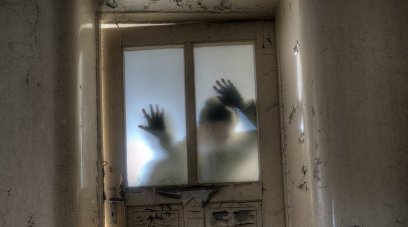 Schatten einer Person hinter einer Glastür, Hände gegen das Glas gedrückt