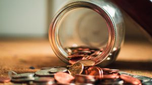 Münzen, halb in einem offenen Glas und halb auf dem Tisch liegen