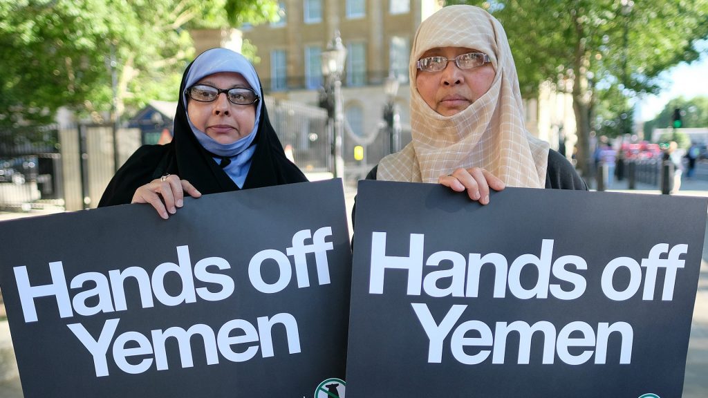 Zwei Frauen mit Kopftüchern tragen schwarze Schilder mit der Aufschrift "Hands off Yemen"