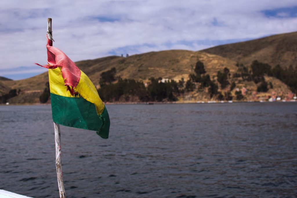 Flagge von Bolivien auf einem Boot, dahinter Wasser
