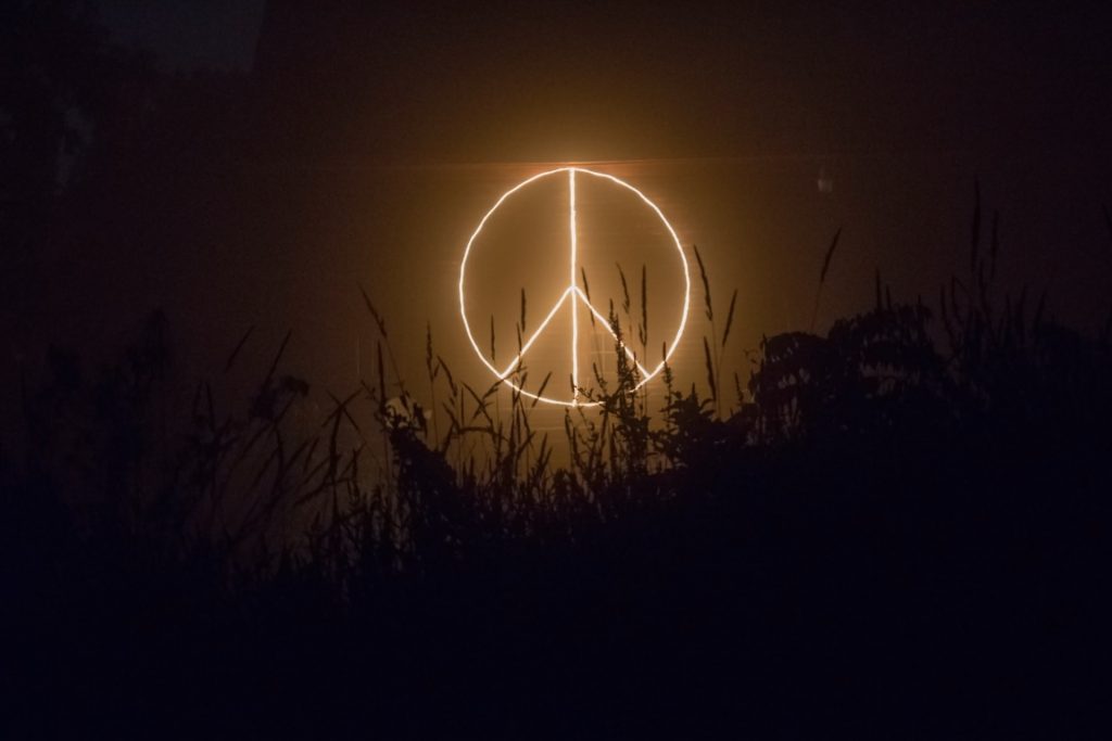 Das Peace-Zeichen in Neon-Farbe auf einen dunklen See projiziert