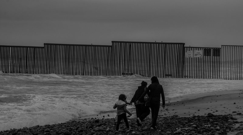 Drei Menschen an der Grenzen zwischen den USA und Mexiko am Meer, im Hintergrund der Grenzzaun