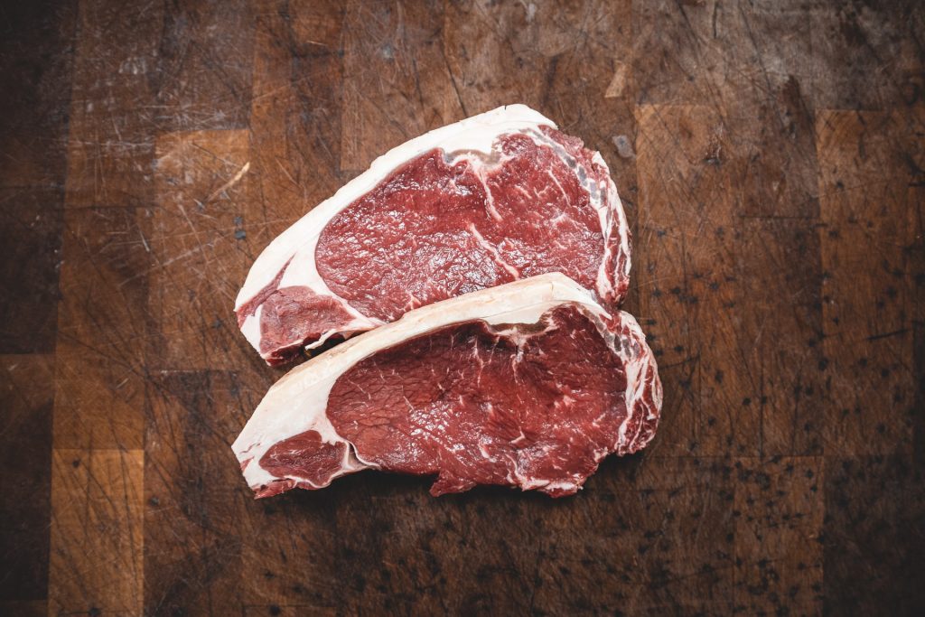Zwei Stücke rohes Fleisch liegen auf einem dunklen Holztisch