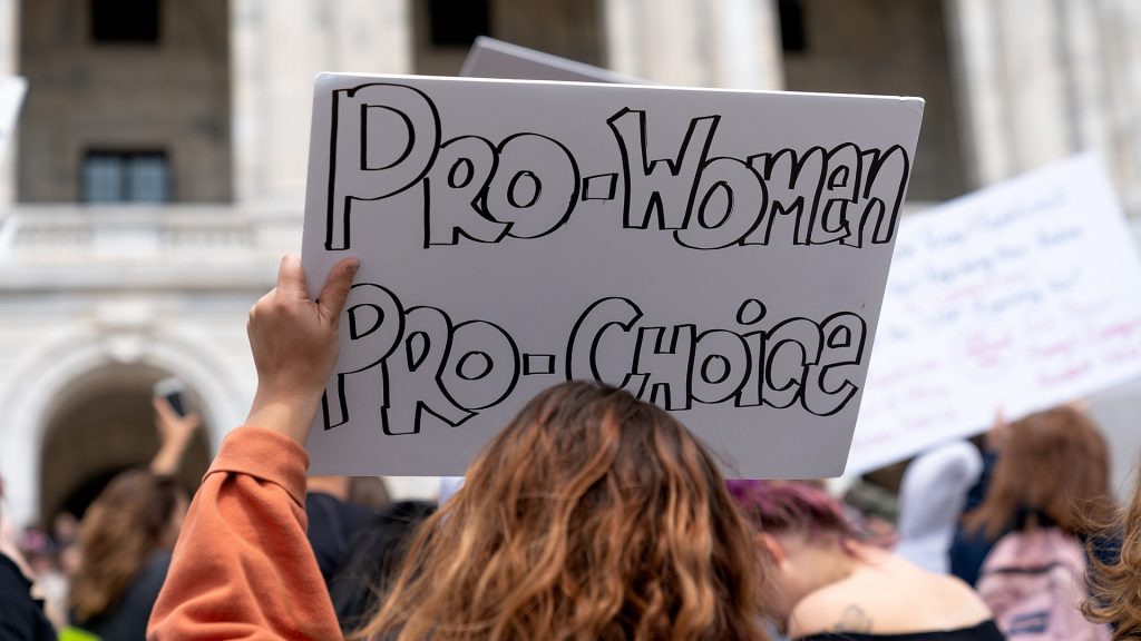 Person hält weißes Schild mit Aufschrift "Pro Women, Pro Choice" in die Höhe, von hinten fotografiert