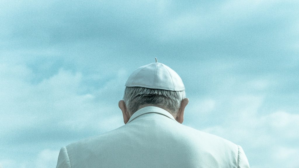 Papst Franziskus von hinten fotografiert, vor ihm wolkiger Himmel