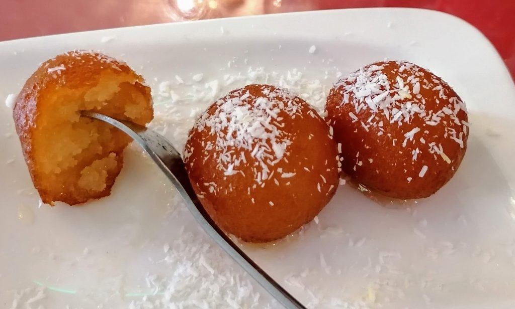 Runde Bällchen als Nachspeise auf einem weißen Teller, in einem Bällchen steckt eine Gabel