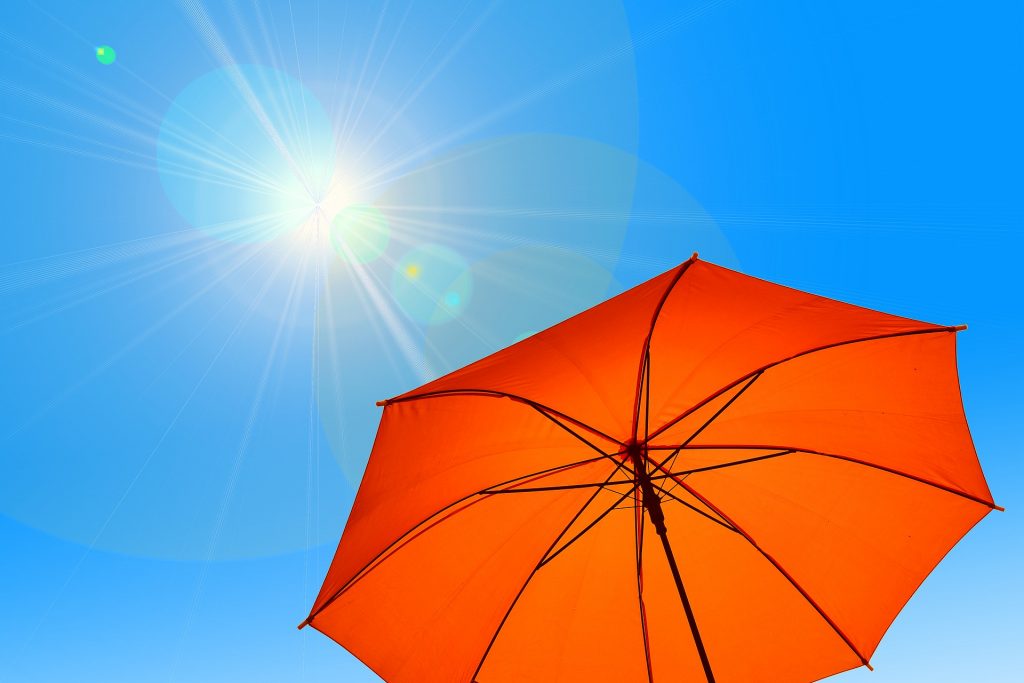 Orangener Regenschirm vor blauem Himmel und strahlendem Sonnenschein