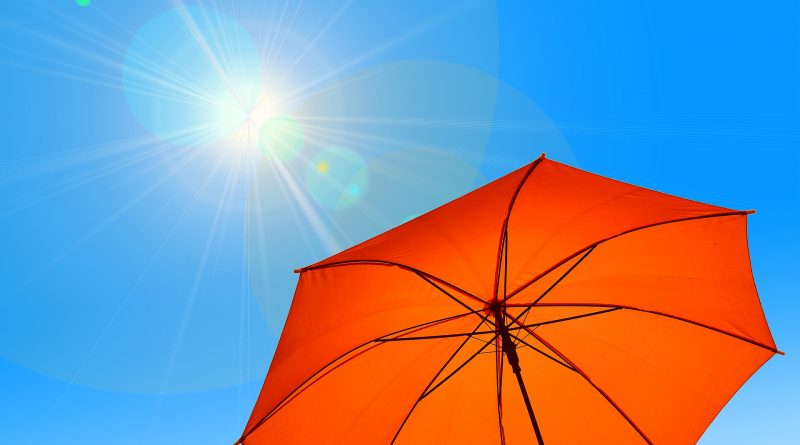 Orangener Regenschirm vor blauem Himmel und strahlendem Sonnenschein