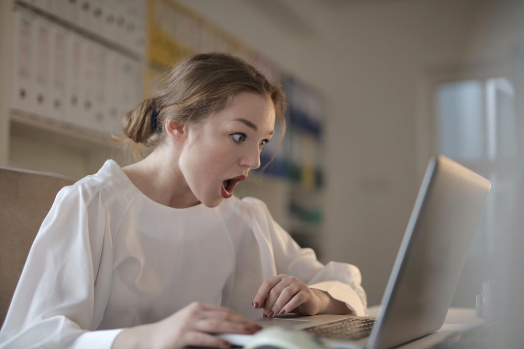 Frau in weißem Shirt starrt mit schockiertem Blick in ihren Laptop