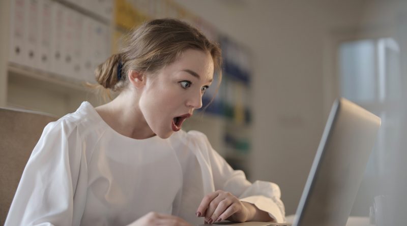 Frau in weißem Shirt starrt mit schockiertem Blick in ihren Laptop