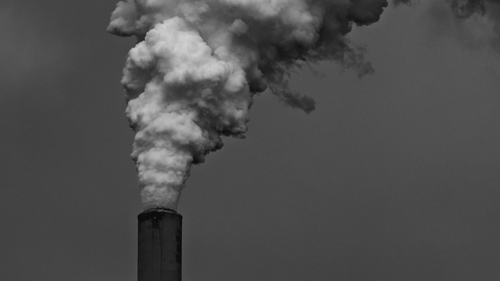 Schwarz-weiß-Foto eines Fabrik-Schornstein, aus dem weißer Raum kommt