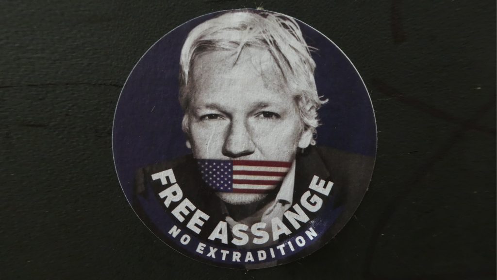 Sticker mit Kopf von Assange mit US-Mundschutz und Text "Free Assange - No Extradition"