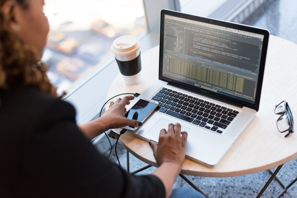 Frau sitzt an einem runden Tisch vor ihrem Laptop und programmiert