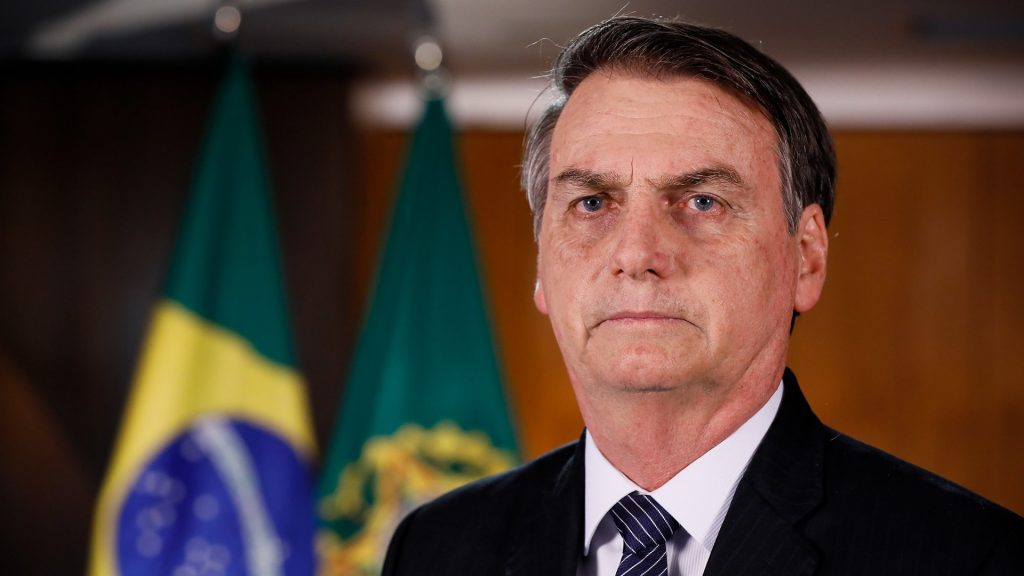 Jair Bolsonaro im schwarzen Anzug vor eine Brasilien-Flagge