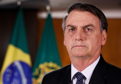 Jair Bolsonaro im schwarzen Anzug vor eine Brasilien-Flagge
