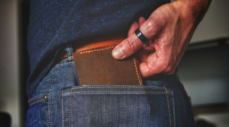 Person hat braune Brieftasche in blauer Jeans stecken und holt diese mit der Hand heraus