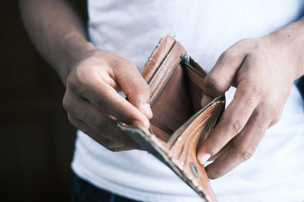 Person mit weißem Shirt hält leere Geldtasche in den Händen