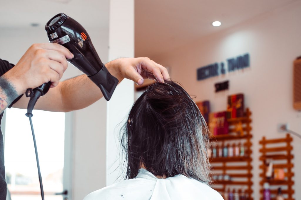 Friseur*in föhnt Person ihre langen, dunklen Haare
