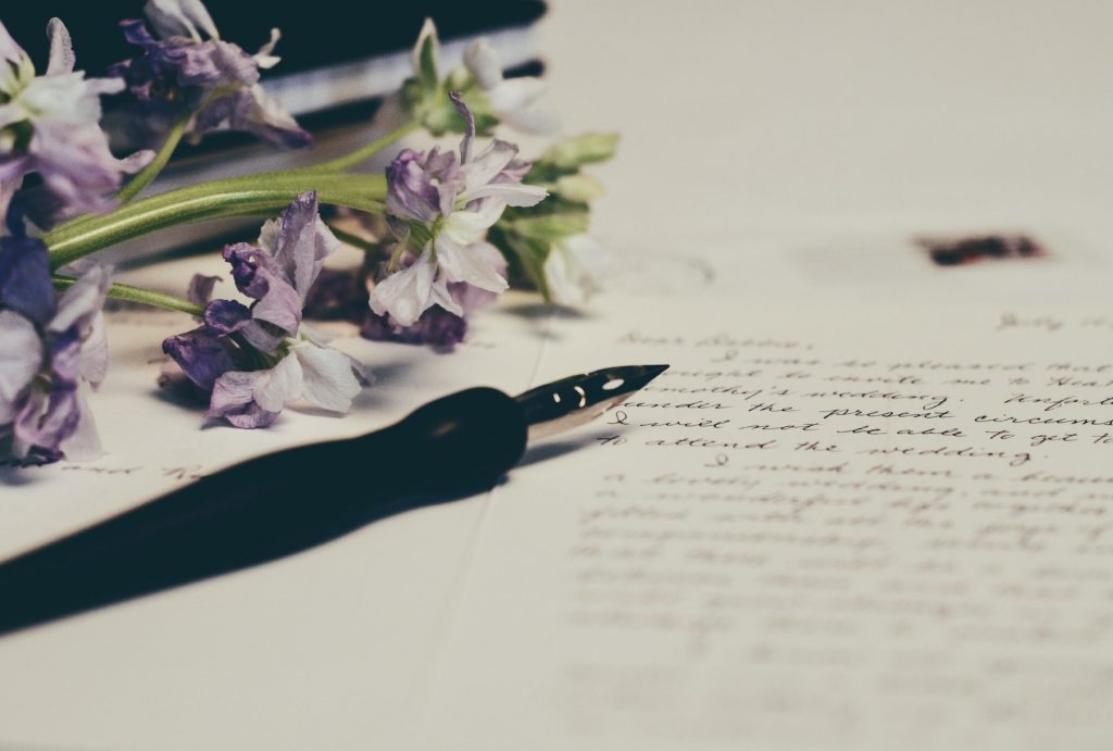 Füllfeder liegt auf weißem Papier mit Text, rechts sieht man Blumen
