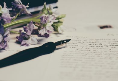 Füllfeder liegt auf weißem Papier mit Text, rechts sieht man Blumen