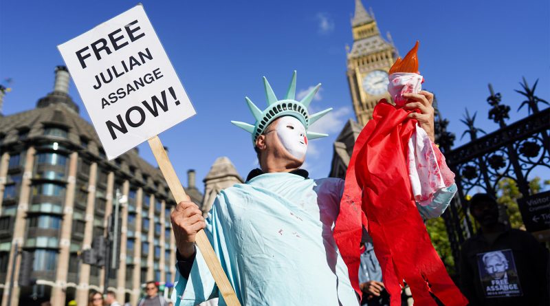 Demonstrant, verkleidet als die Freiheitsstatue, hält ein Schild mit der Aufschrift "Free Julian Assange Now" in die Höhe.