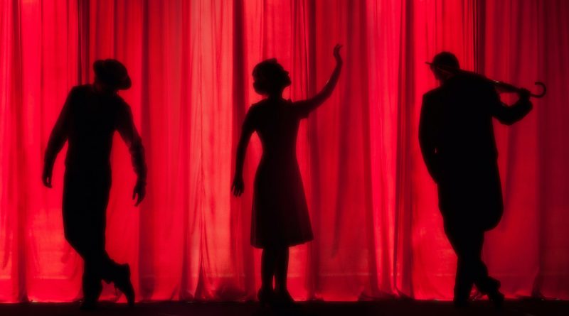 Drei schwarze Silhouetten hinter einem roten Theater-Vorhang
