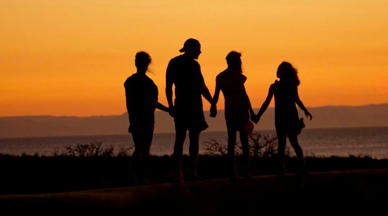 Vier Personen als Silhouetten vor einem Sonnenuntergang halten sich an den Händen