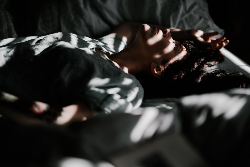 Person liegt im Bett, es ist dunkel, Lichtstreifen fallen auf ihr Gesicht