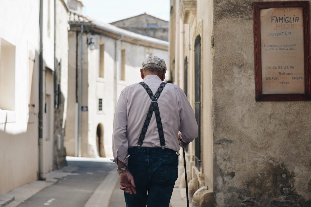 Älterer Mann mit Hemd, Hosenträger und Stock in einer schmalen Gasse, von hinten fotografiert