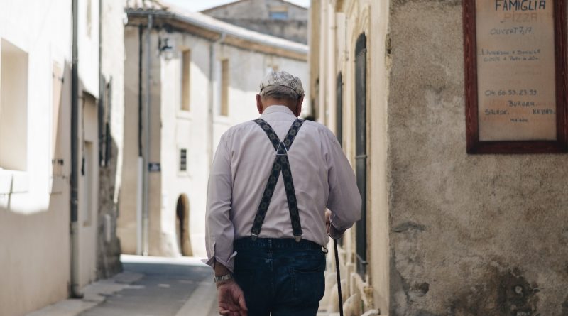 Älterer Mann mit Hemd, Hosenträger und Stock in einer schmalen Gasse, von hinten fotografiert