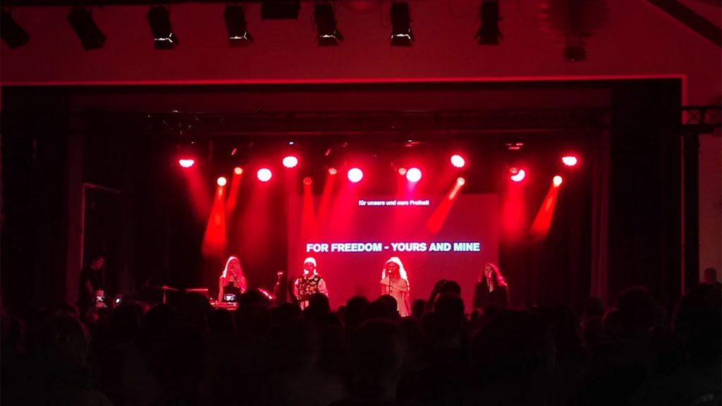 Pussy Riot auf der Bühne, rotes Licht, rundherum alles dunkel